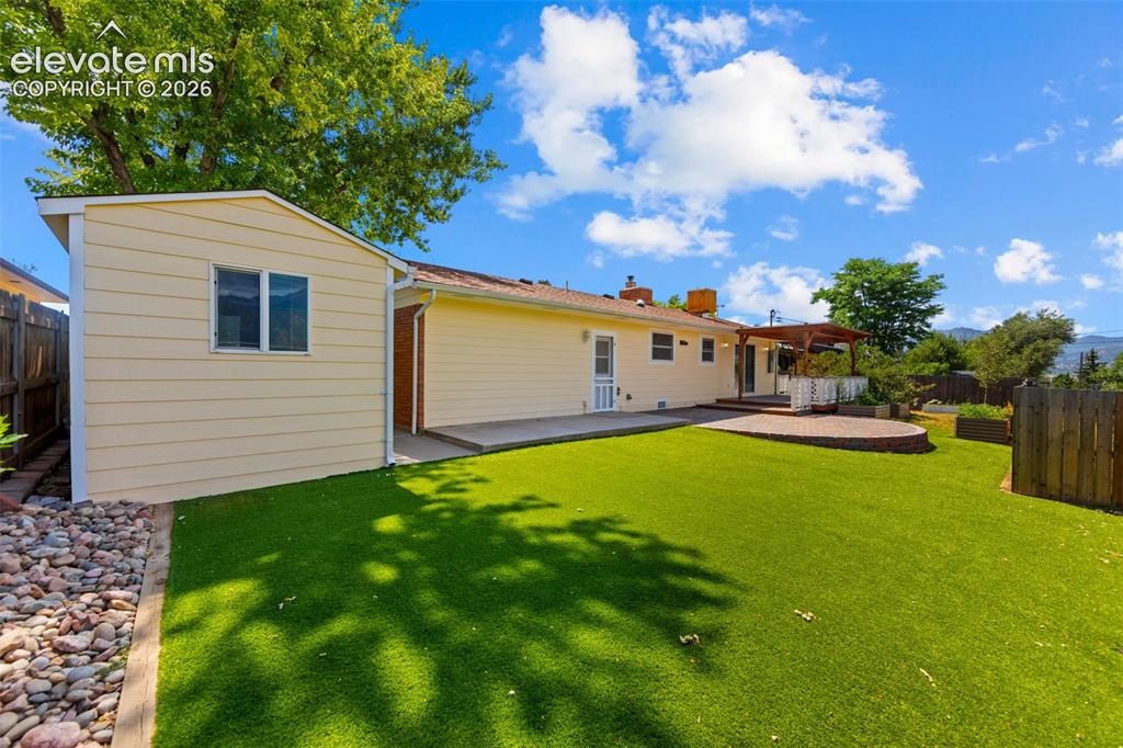 Image 24 of 34: Expansive backyard featuring artificial turf, a circular paver patio, and a