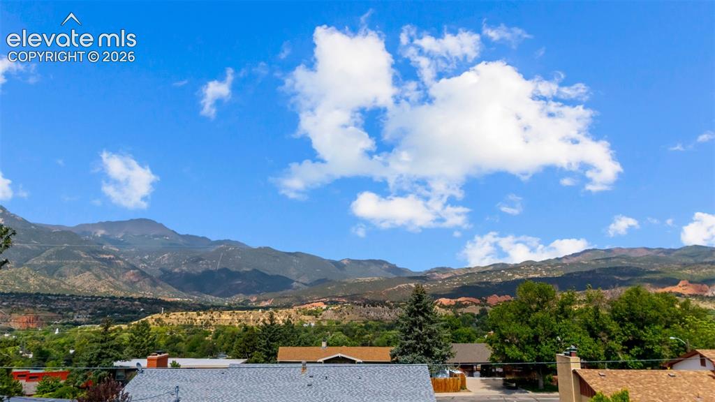 Image 32 of 34: Mountain backdrop with distant red rock formations and a vibrant green tree