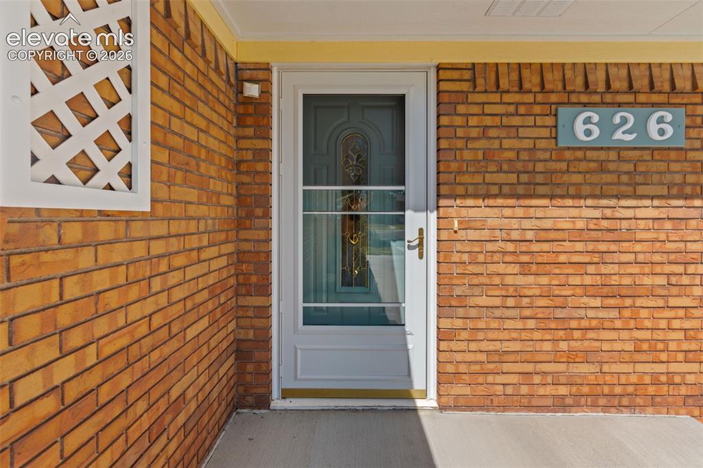 Image 4 of 34: Brick exterior featuring a storm door, an ornate entry door, and a concrete