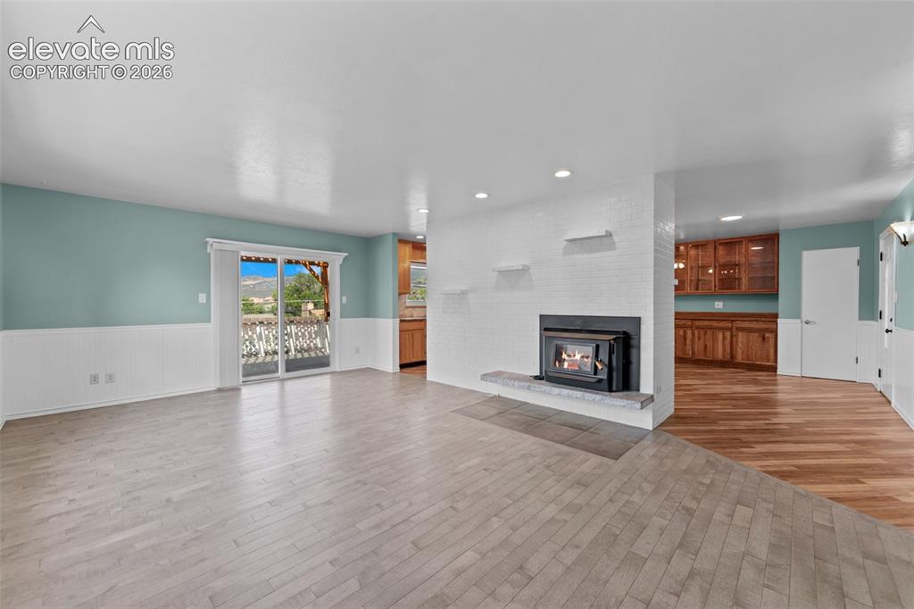 Image 9 of 34: Spacious living area featuring light wood-finish flooring and a white wains