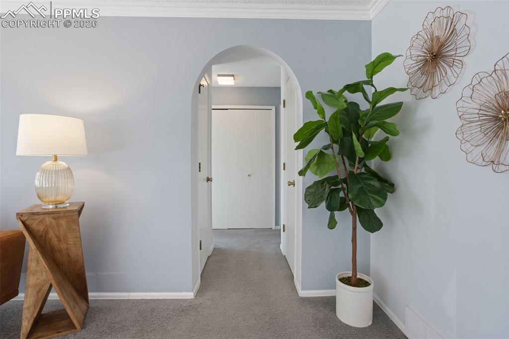 Image 11 of 31: Hallway with arched walkways, carpet floors, and ornamental molding
