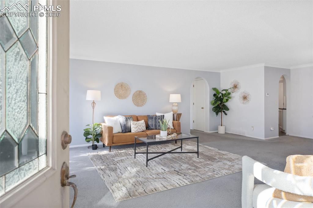 Image 6 of 31: Living area with arched walkways, carpet, and crown molding