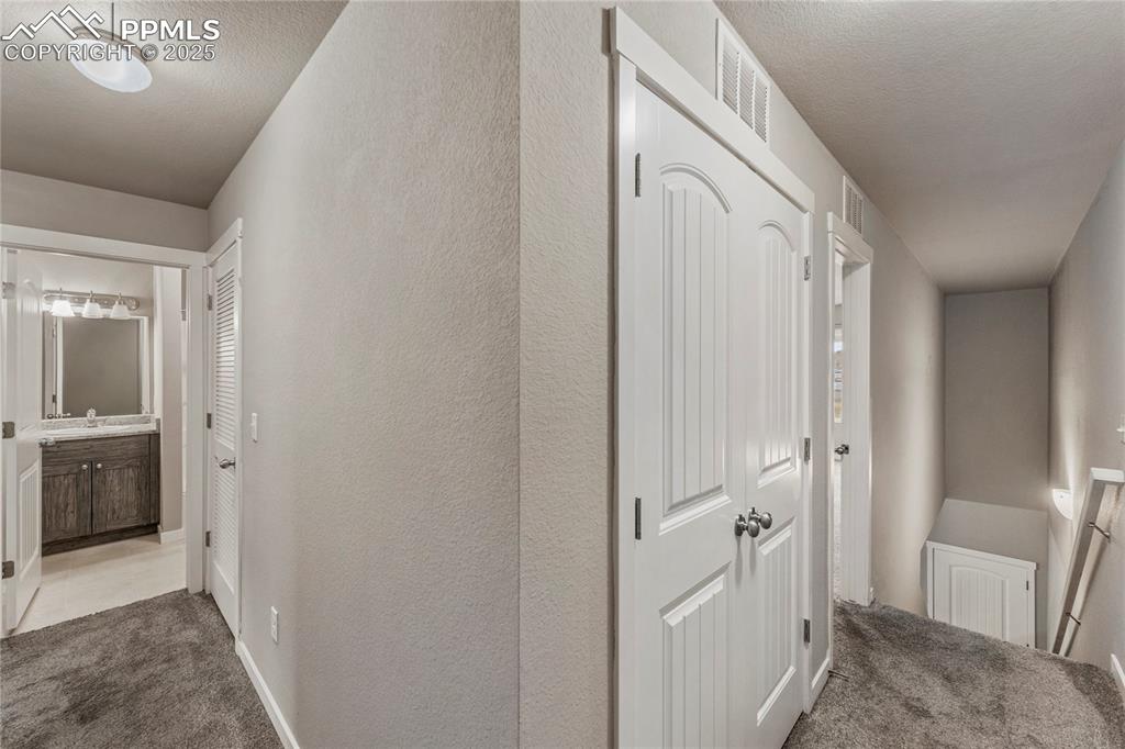Image 15 of 29: Hallway with light carpet, a textured ceiling, and a textured wall