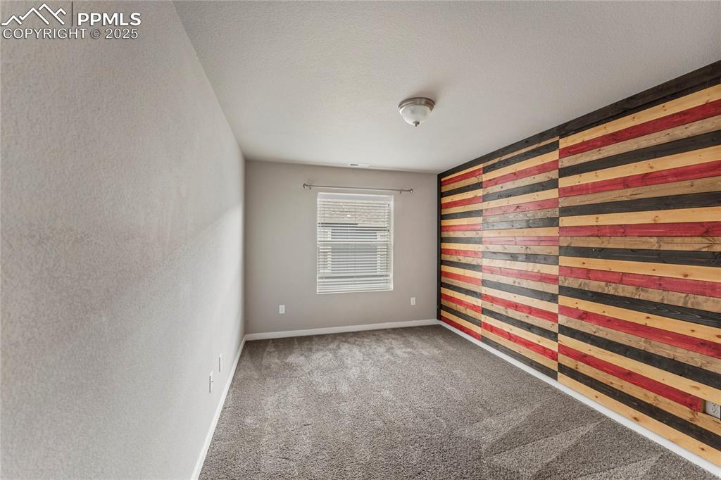 Image 24 of 29: Unfurnished room featuring wooden walls, light carpet, a textured wall, and
