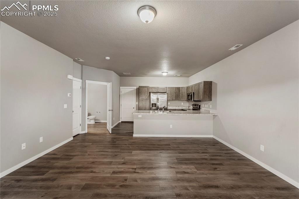 Image 8 of 29: Unfurnished living room featuring a textured ceiling and dark wood-type flo