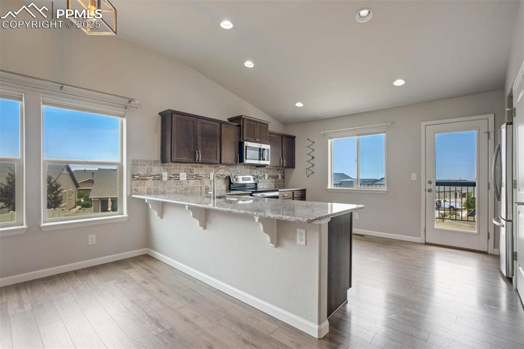 Image 11 of 45: Kitchen featuring dark brown cabinetry, a peninsula, a breakfast bar, stain