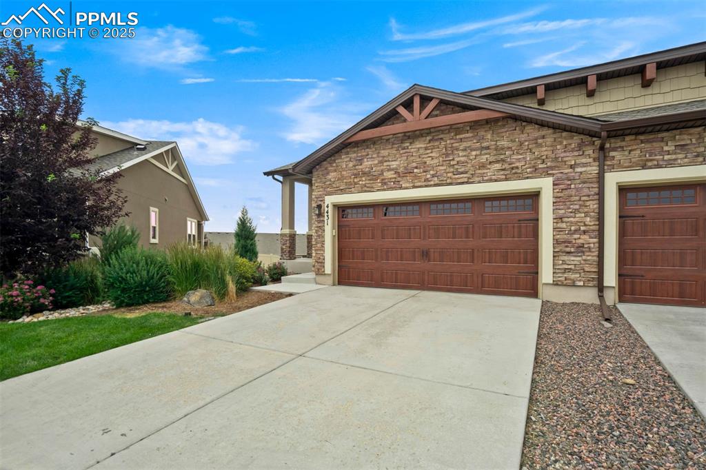 Image 45 of 45: View of side of property with concrete driveway, stone siding, and an attac