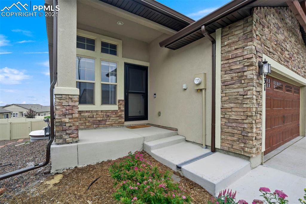 Image 5 of 45: Doorway to property featuring stone siding, stucco siding, and a garage