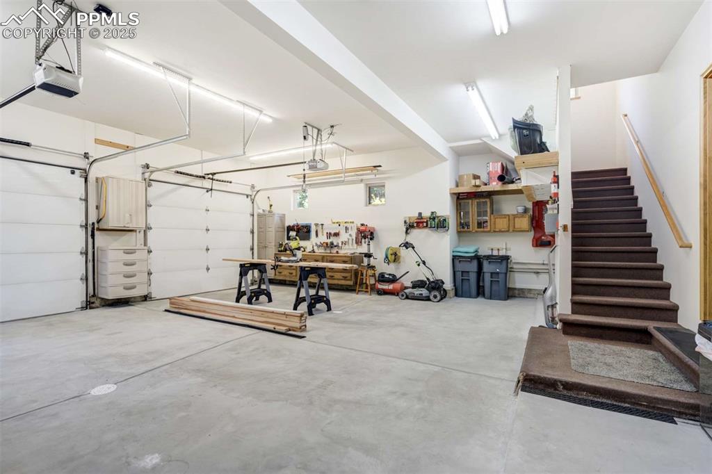 Image 41 of 50: Garage with a workshop area and a garage door opener. Also shows stairs to