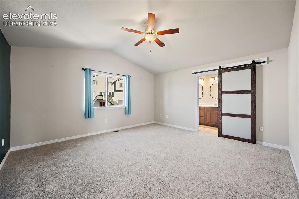 Image 18 of 49: Vaulted ceiling, ceiling fan, carpet flooring, sliding barn door, and a win