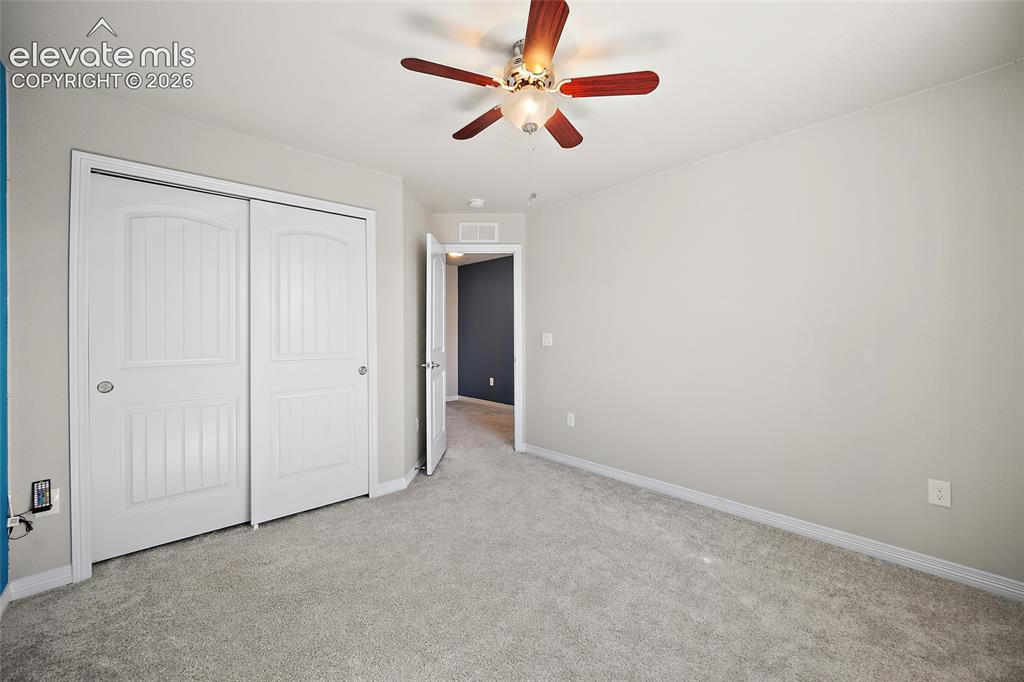 Image 27 of 49: Plush carpet flooring, wood-finish ceiling fan, and white paneled bi-fold c