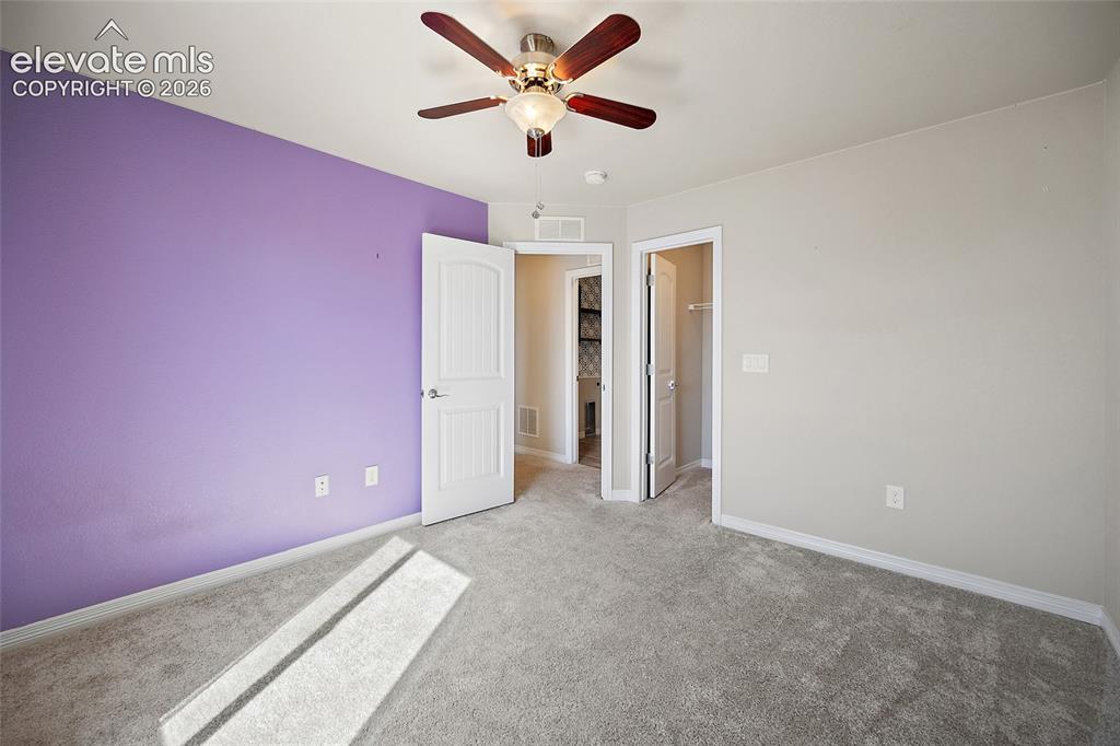 Image 28 of 49: Plush gray carpeting, a ceiling fan with wood-finish blades, and a paneled 