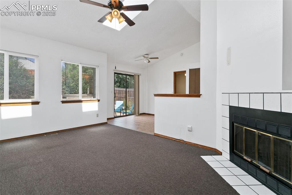 Image 2 of 24: Unfurnished living room with lofted ceiling, light carpet, a tiled fireplac