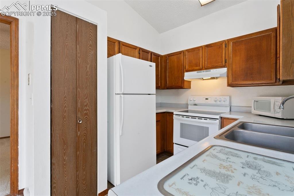 Image 3 of 24: Kitchen with white appliances, light countertops, brown cabinetry, under ca