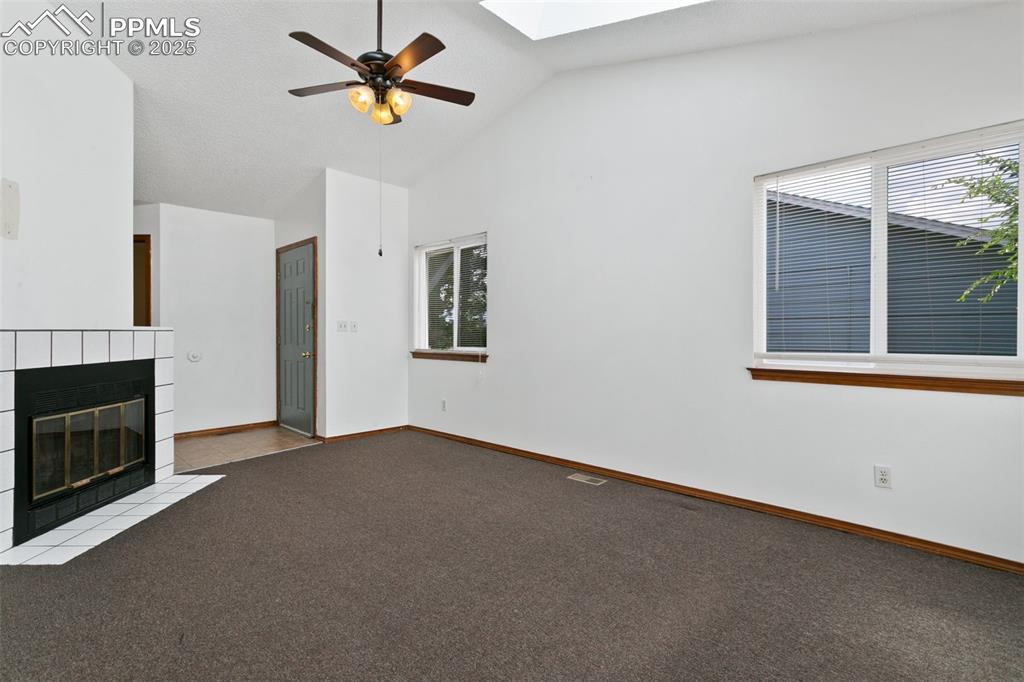 Image 9 of 24: Unfurnished living room with a skylight, carpet, ceiling fan, a tile firepl