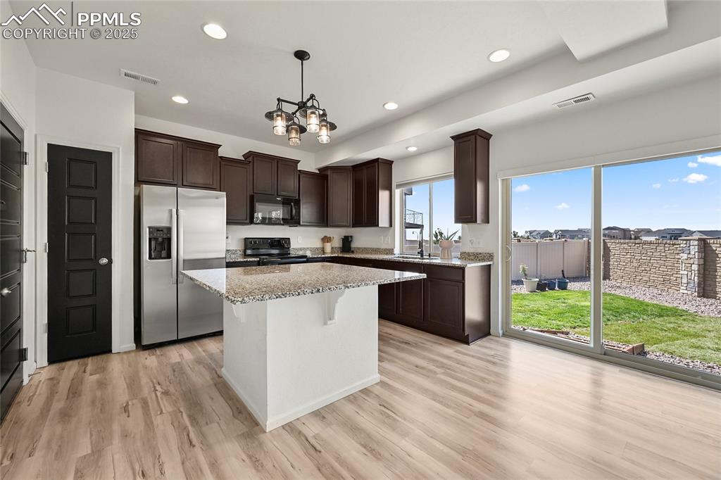 Image 10 of 28: Kitchen featuring dark brown cabinetry, black appliances, light stone count