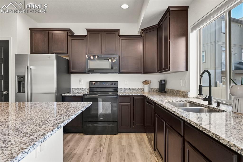 Image 11 of 28: Kitchen featuring black appliances, dark brown cabinetry, light wood-type f