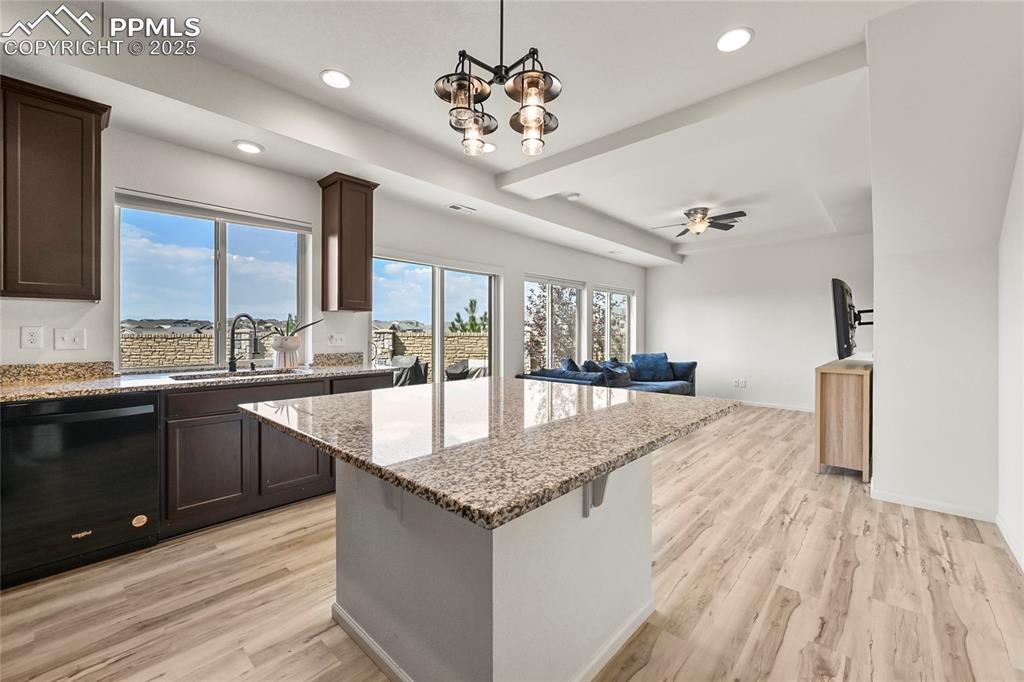 Image 12 of 28: Kitchen with dishwasher, light stone counters, open floor plan, dark brown
