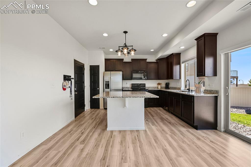 Image 9 of 28: Kitchen with pendant lighting, dark brown cabinets, light wood finished flo
