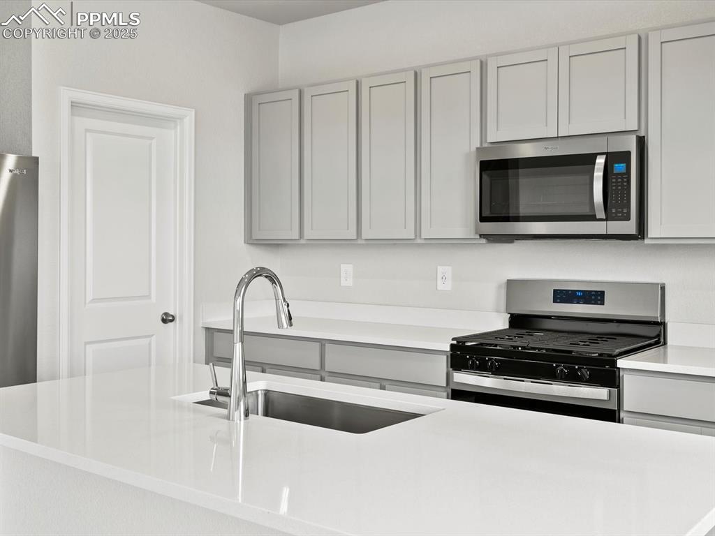 Image 3 of 28: Kitchen featuring gray cabinets, stainless steel appliances, and light coun