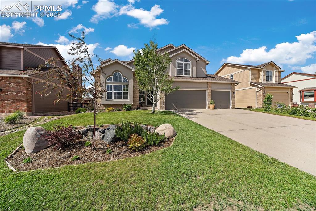 Caption: View of front facade featuring an attached garage, driveway, a front lawn, and stucco siding