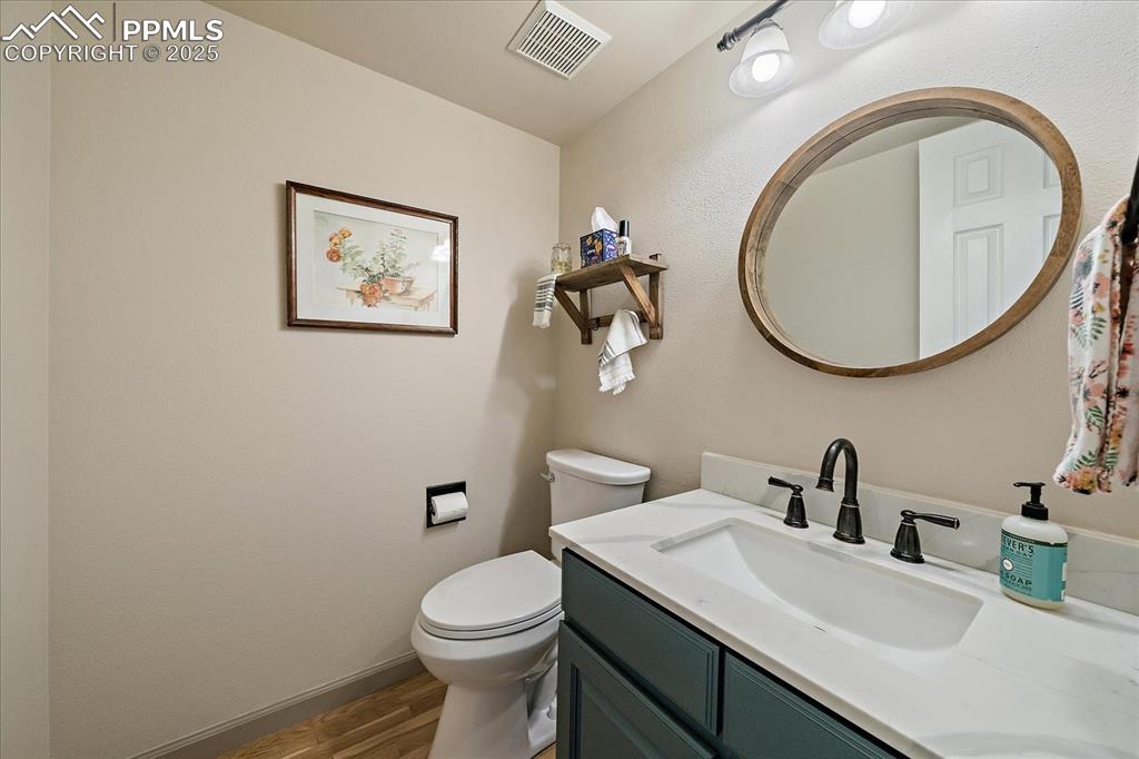 Image 21 of 47: Half bath featuring wood finished floors, toilet, vanity, and baseboards