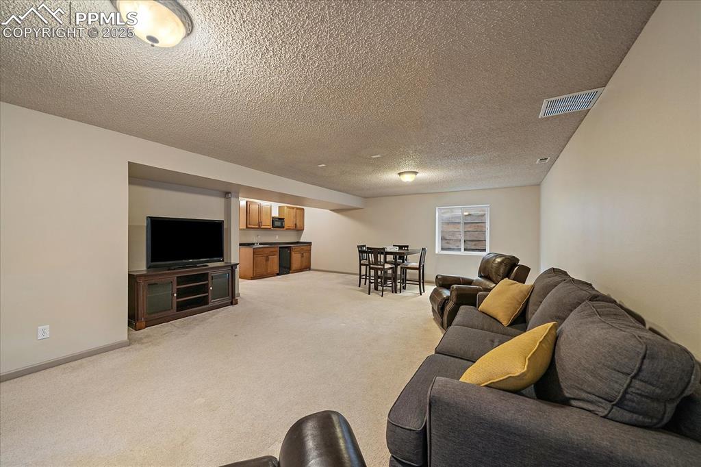Image 34 of 47: Living room with light colored carpet, a textured ceiling, and baseboards
