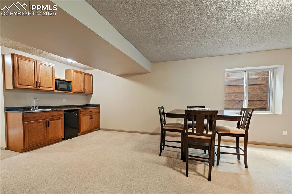 Image 38 of 47: Dining room featuring bar with sink, a textured ceiling, light carpet, and 