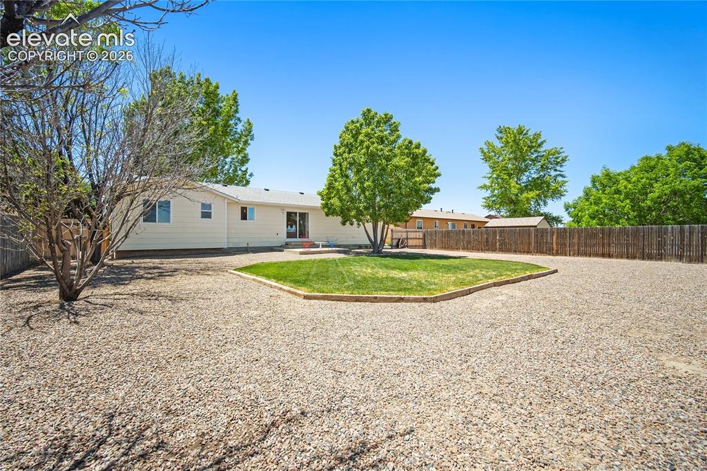 Image 23 of 29: Expansive gravel yard with a central grassy area and mature trees
