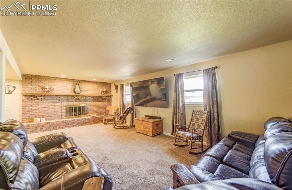 Image 21 of 25: Carpeted living room featuring a brick fireplace, a textured ceiling, and b