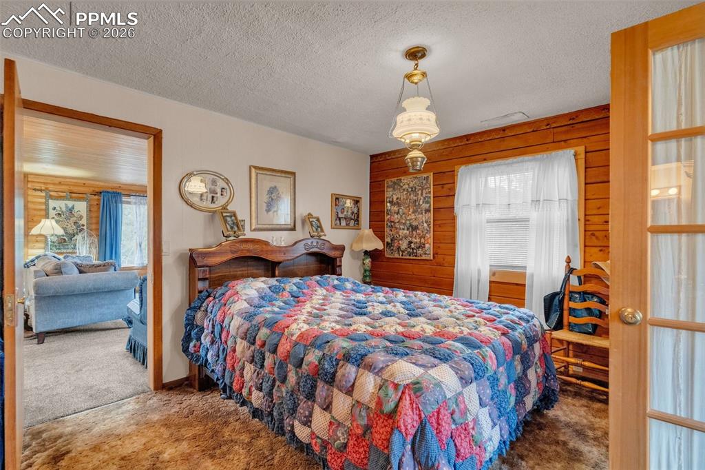 Image 19 of 41: Bedroom featuring a wood-paneled accent wall and textured wall-to-wall carp