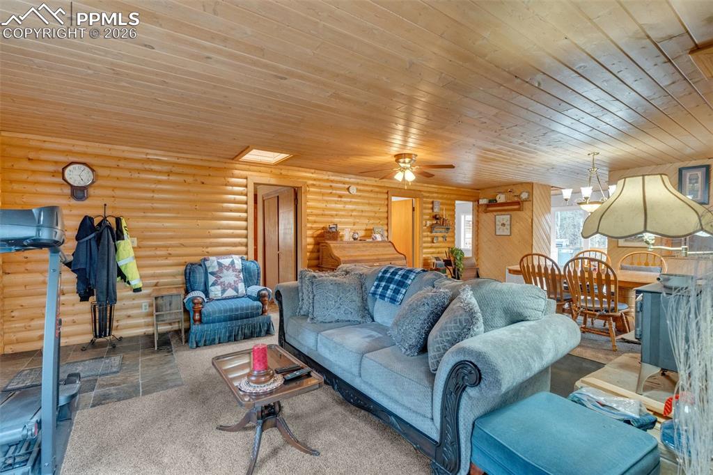 Image 7 of 41: Open-concept living area featuring log walls, wood-paneled ceilings, and sl