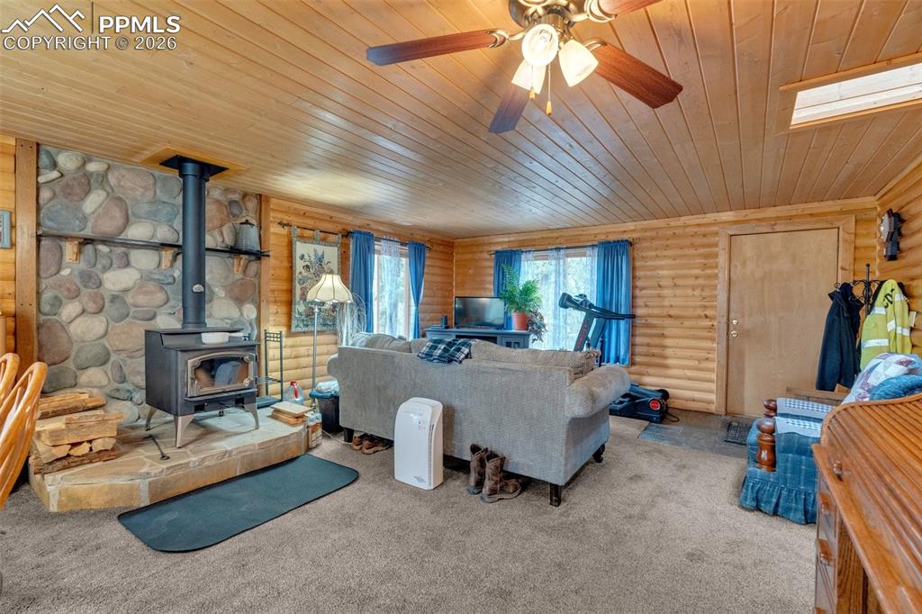 Image 8 of 41: Living area with wood-paneled walls and ceiling, featuring a stone fireplac