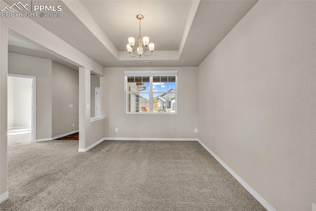 Image 10 of 44: Empty room with carpet, a raised ceiling, and a chandelier