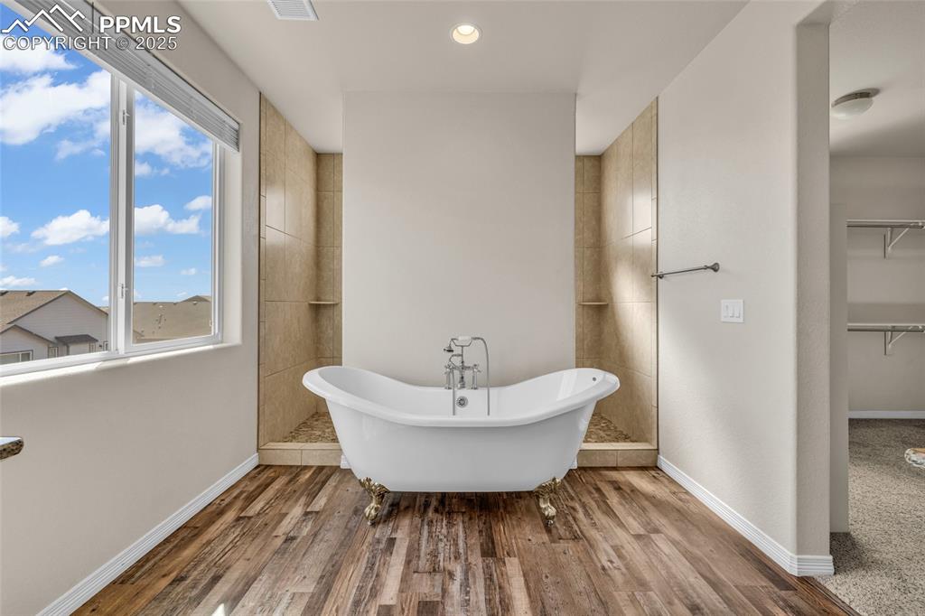 Image 23 of 44: Bathroom featuring a freestanding tub, a walk in closet, wood finished floo