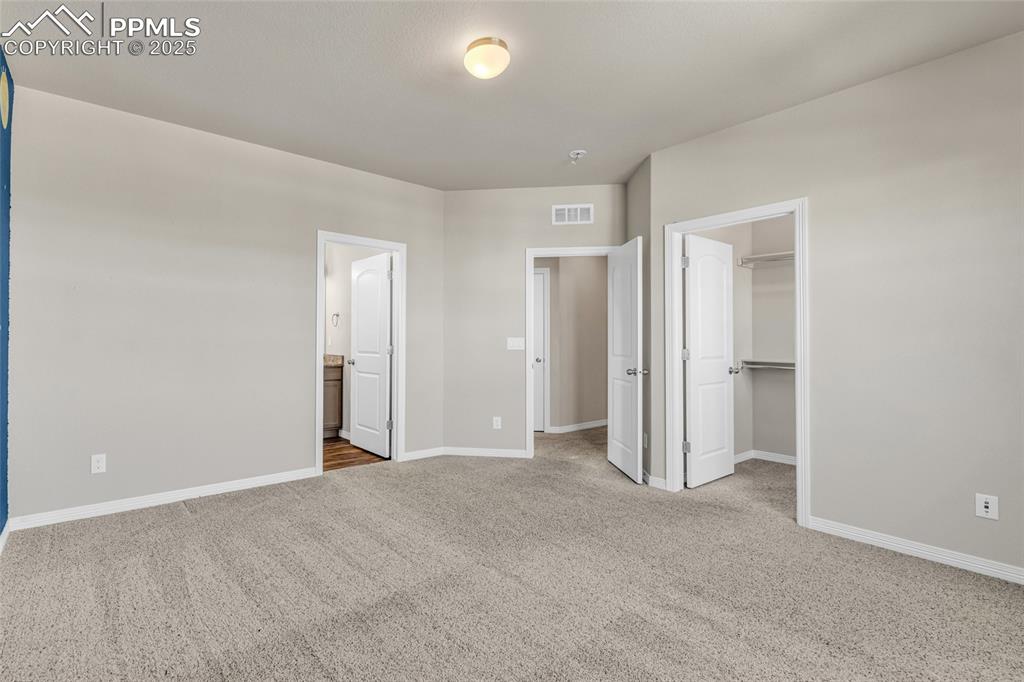Image 31 of 44: Unfurnished bedroom featuring a spacious closet, light carpet, and ensuite 