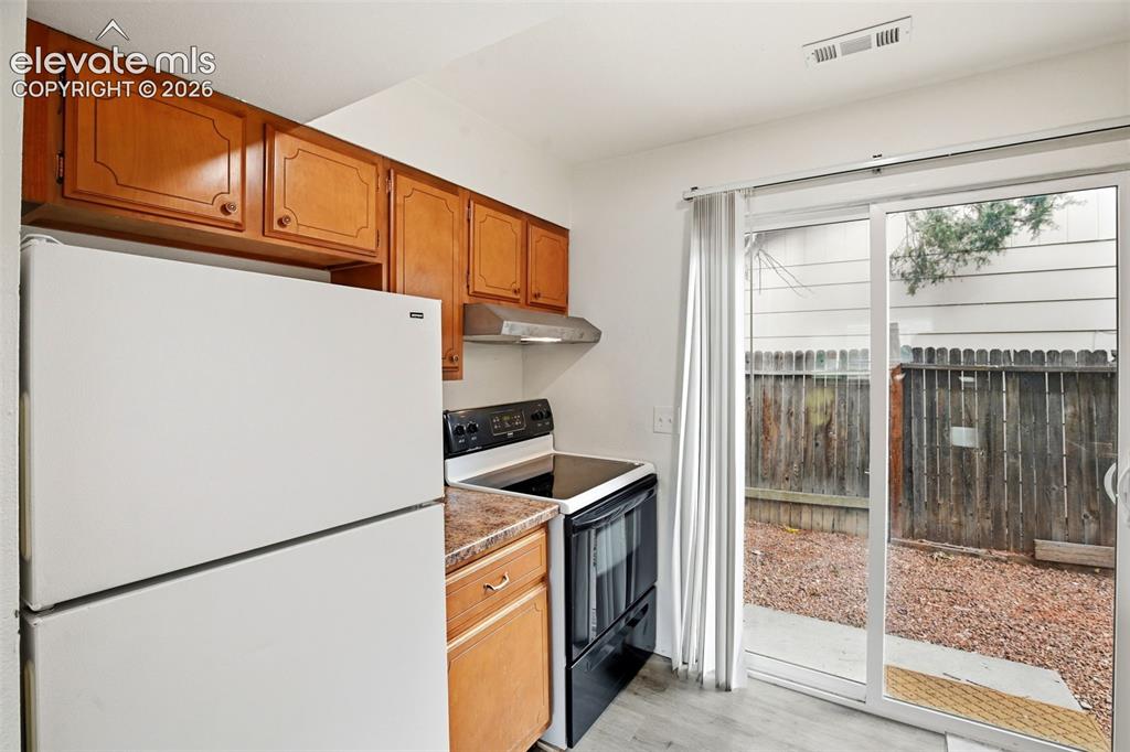 Image 12 of 31: Kitchen with wood-finish cabinetry, white refrigerator, black range, and st