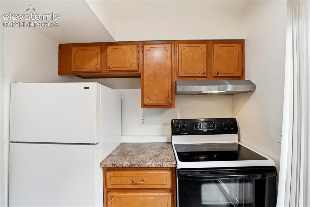 Image 13 of 31: Wood-finish cabinetry, built-in range hood, white refrigerator, and black e