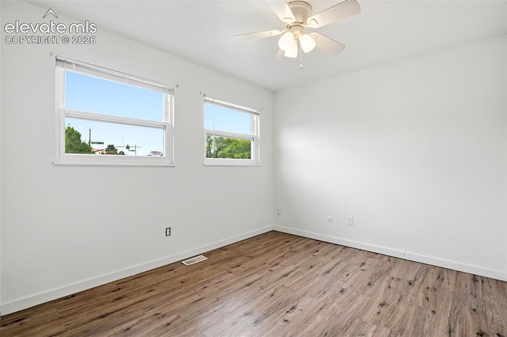 Image 27 of 31: Wood-finish flooring, white walls, two windows, and a ceiling fan with inte