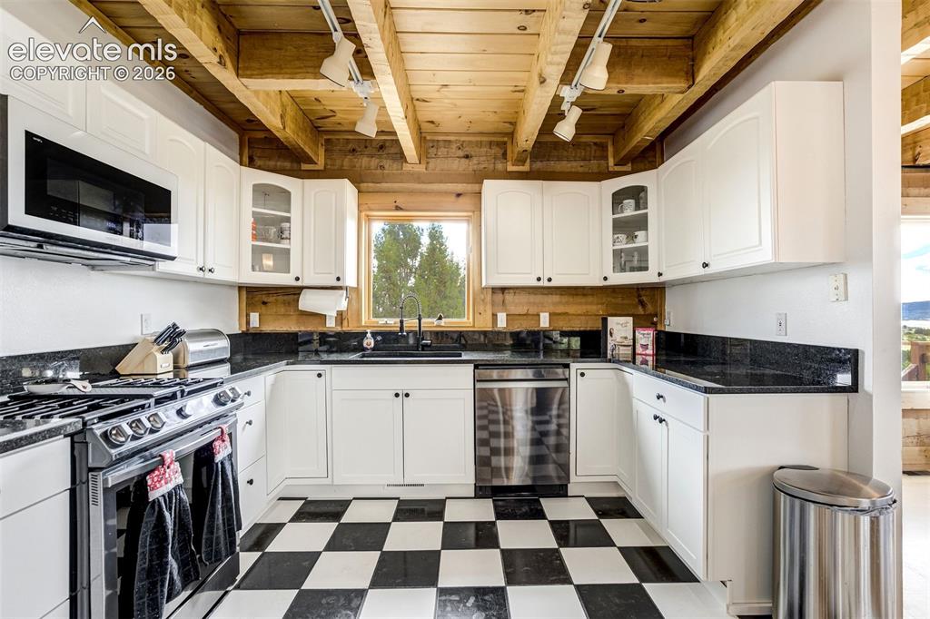 Image 16 of 50: U-shaped kitchen featuring white cabinetry, black countertops, stainless st