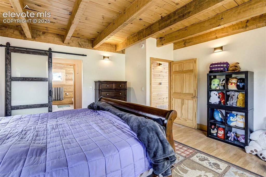 Image 18 of 50: Wood-beamed ceiling with exposed trusses, wood-finish flooring, and light-t