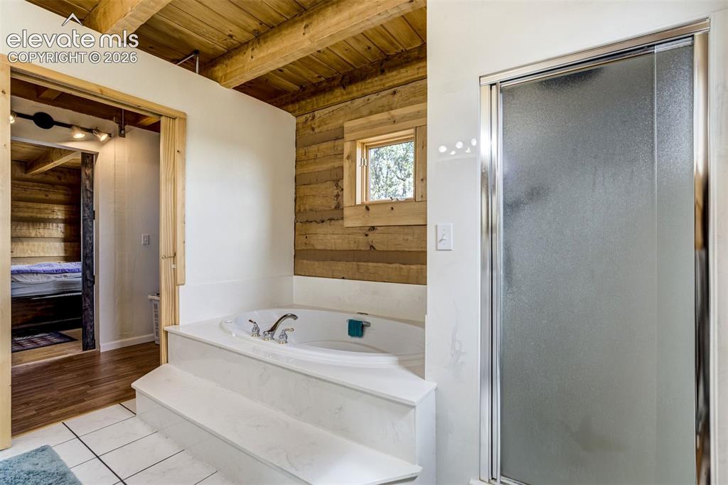 Image 22 of 50: Soaking tub with built-in steps, adjacent to a frosted glass shower enclosu