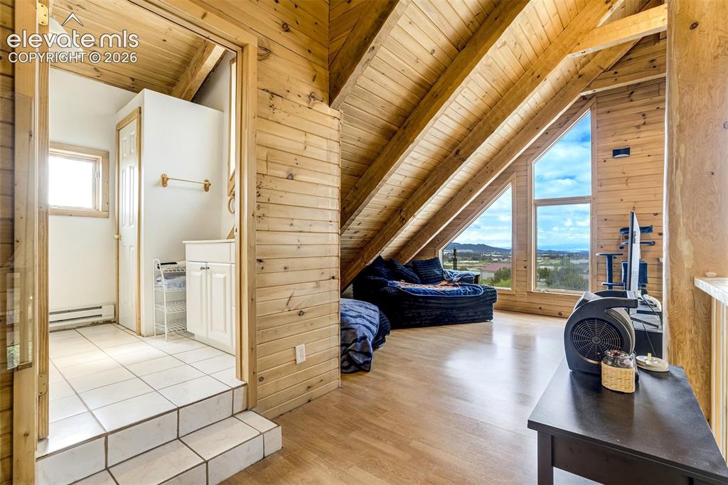 Image 34 of 50: Wood-paneled walls and ceiling beams complement a spacious room with wood-f