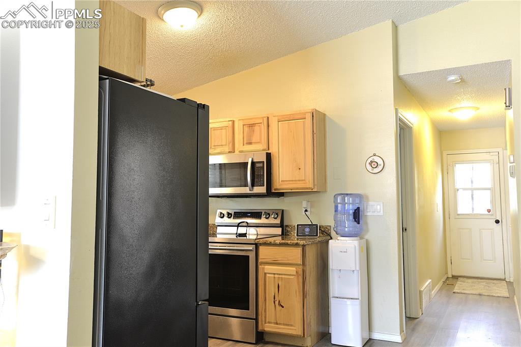 Image 13 of 29: Kitchen with stainless steel appliances, a textured ceiling, light wood-sty