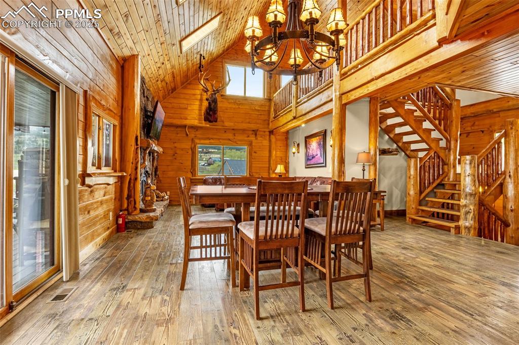 Image 11 of 45: Dining space featuring a chandelier, high vaulted ceiling, wooden walls, st