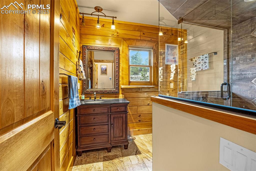 Image 14 of 45: Bathroom featuring vanity, tiled shower, stone finish floors, and wood wall