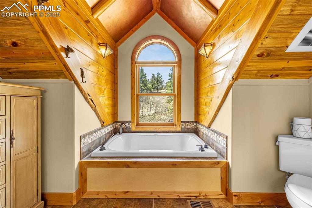 Image 27 of 45: Bathroom featuring toilet, vaulted ceiling, a garden tub, and baseboards