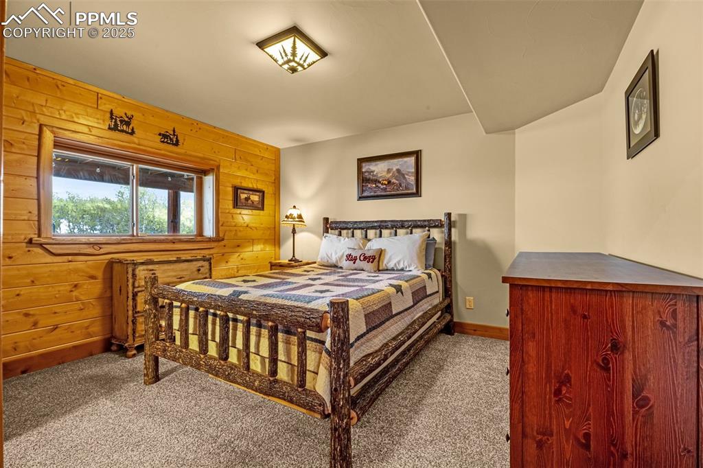 Image 32 of 45: Bedroom with carpet flooring, wood walls, and baseboards