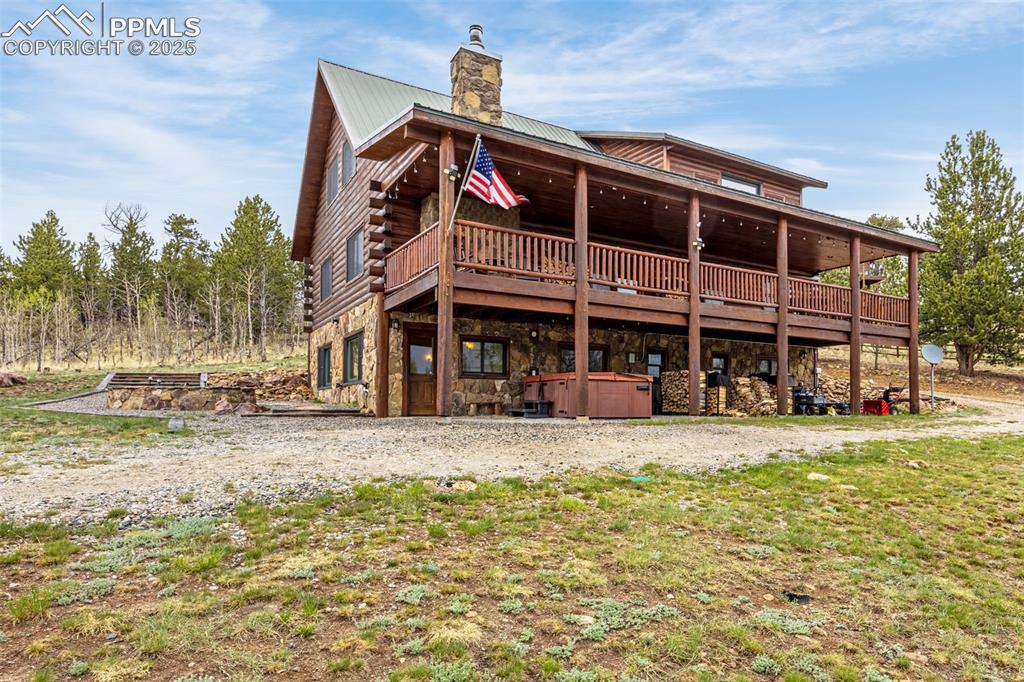 Image 38 of 45: Back of house with a hot tub, stone siding, a chimney, a wooden deck, and m