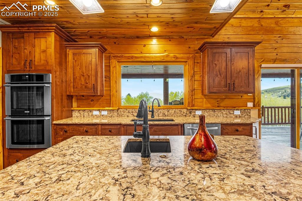 Image 9 of 45: Kitchen with stainless steel appliances, wooden ceiling, a sink, brown cabi